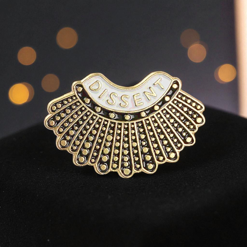 Decorative brooch with 'DISSENT' text on a dark background