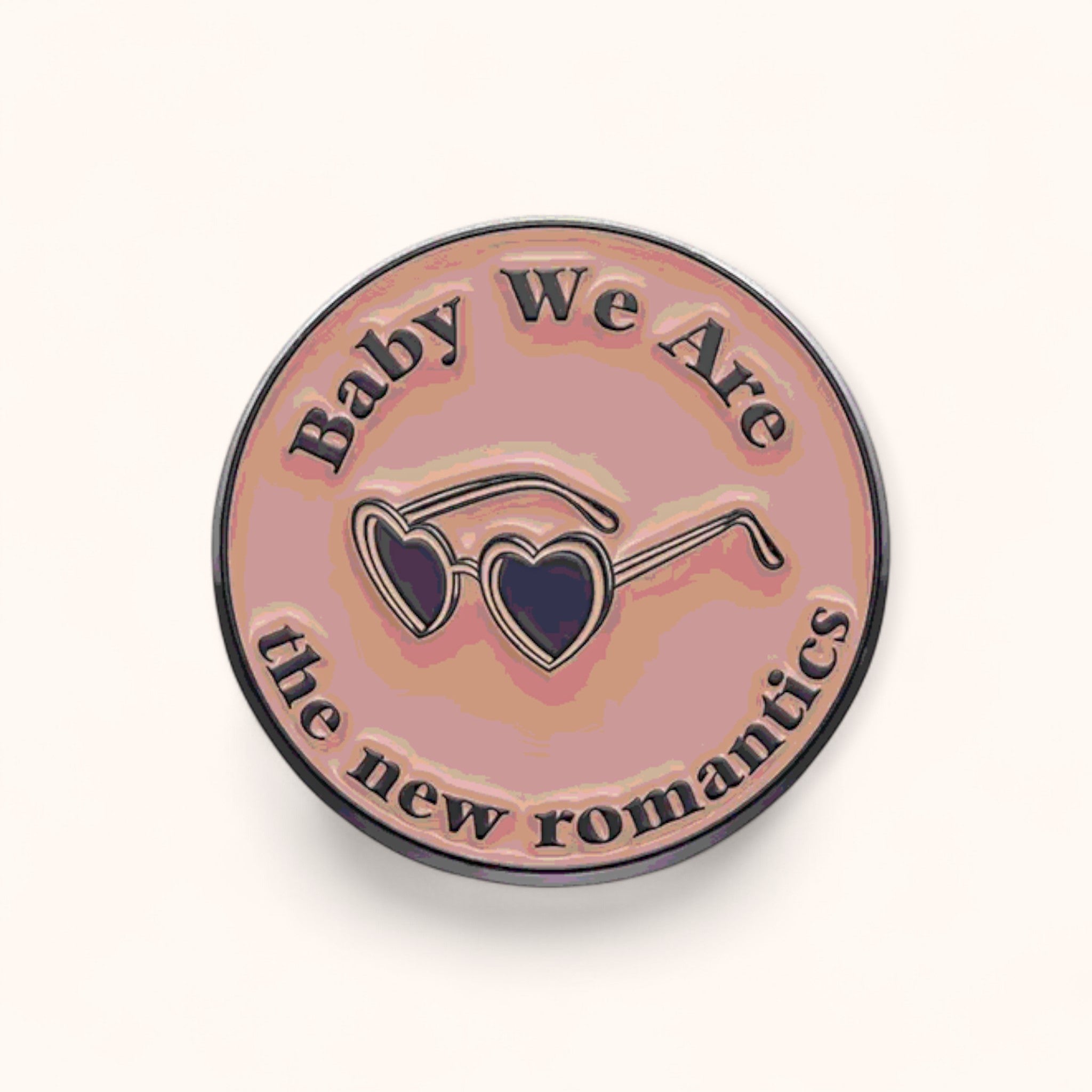 Round enamel pin with sunglasses design and text 'Baby We Are the new romantics' on a pink background