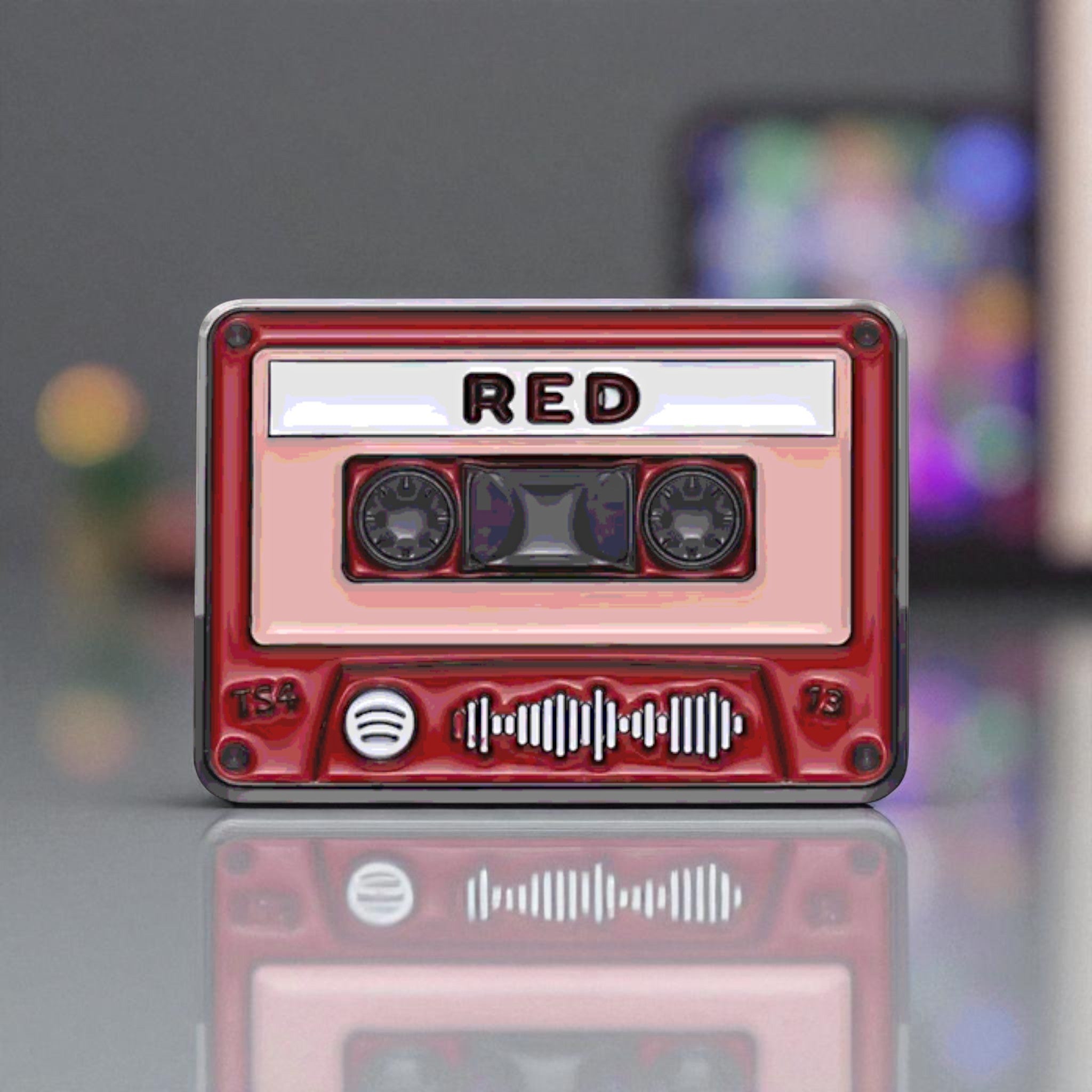 Red cassette tape-shaped enamel pinn with 'RED' branding on a reflective surface.
