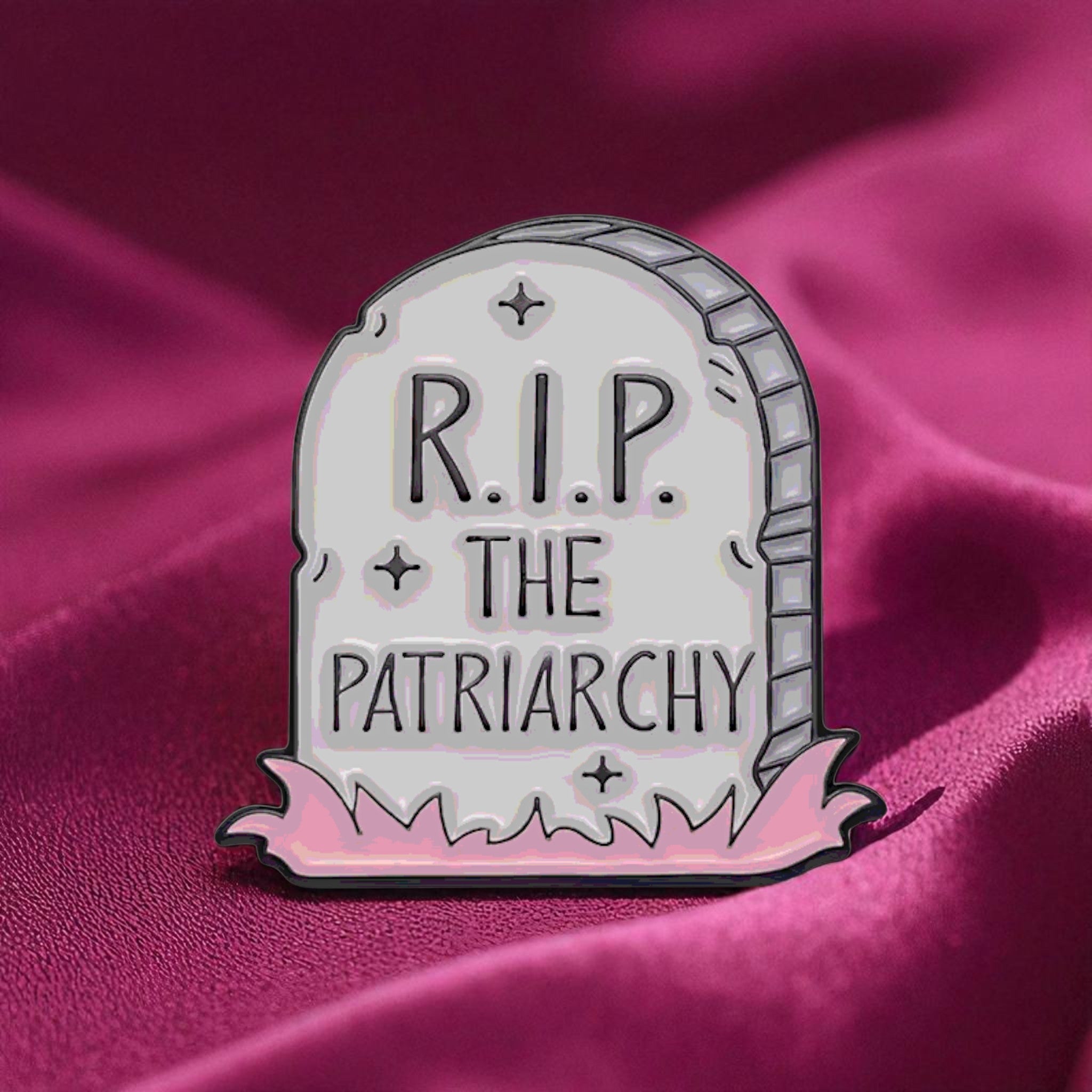 Enamel pin shaped like a tombstone with 'R.I.P. THE PATRIARCHY' text on a pink background