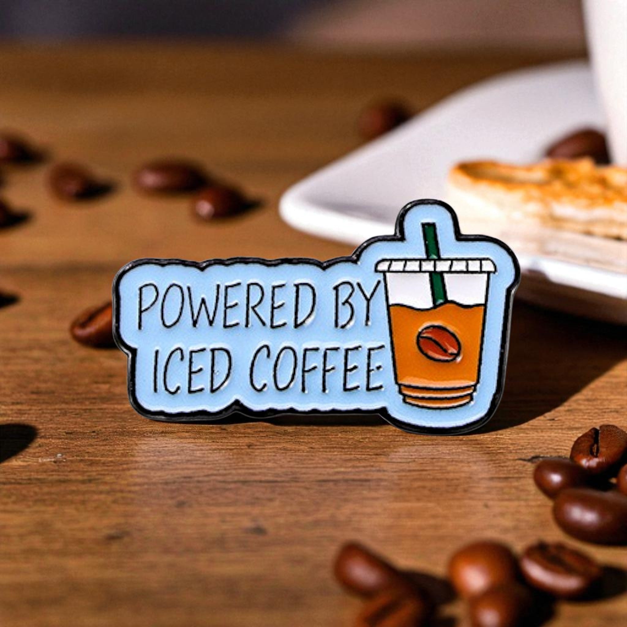 Enamel pin with 'Powered by Iced Coffee' text 