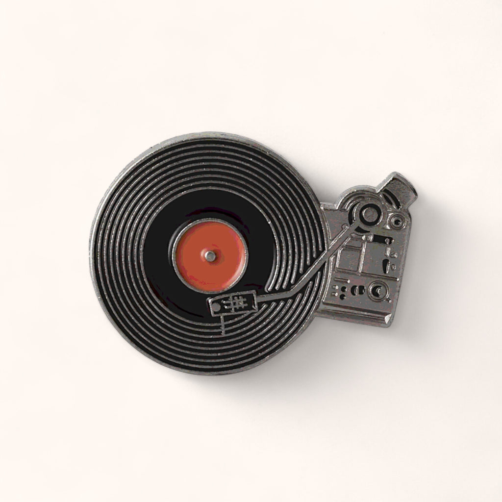 Black enamel pin shaped like a vintage record player with a spinning vinyl record.